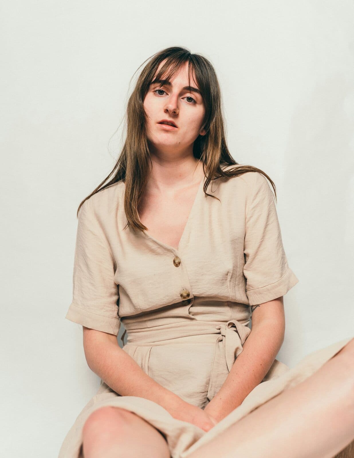 Woman in a linen dress sitting against a white wall