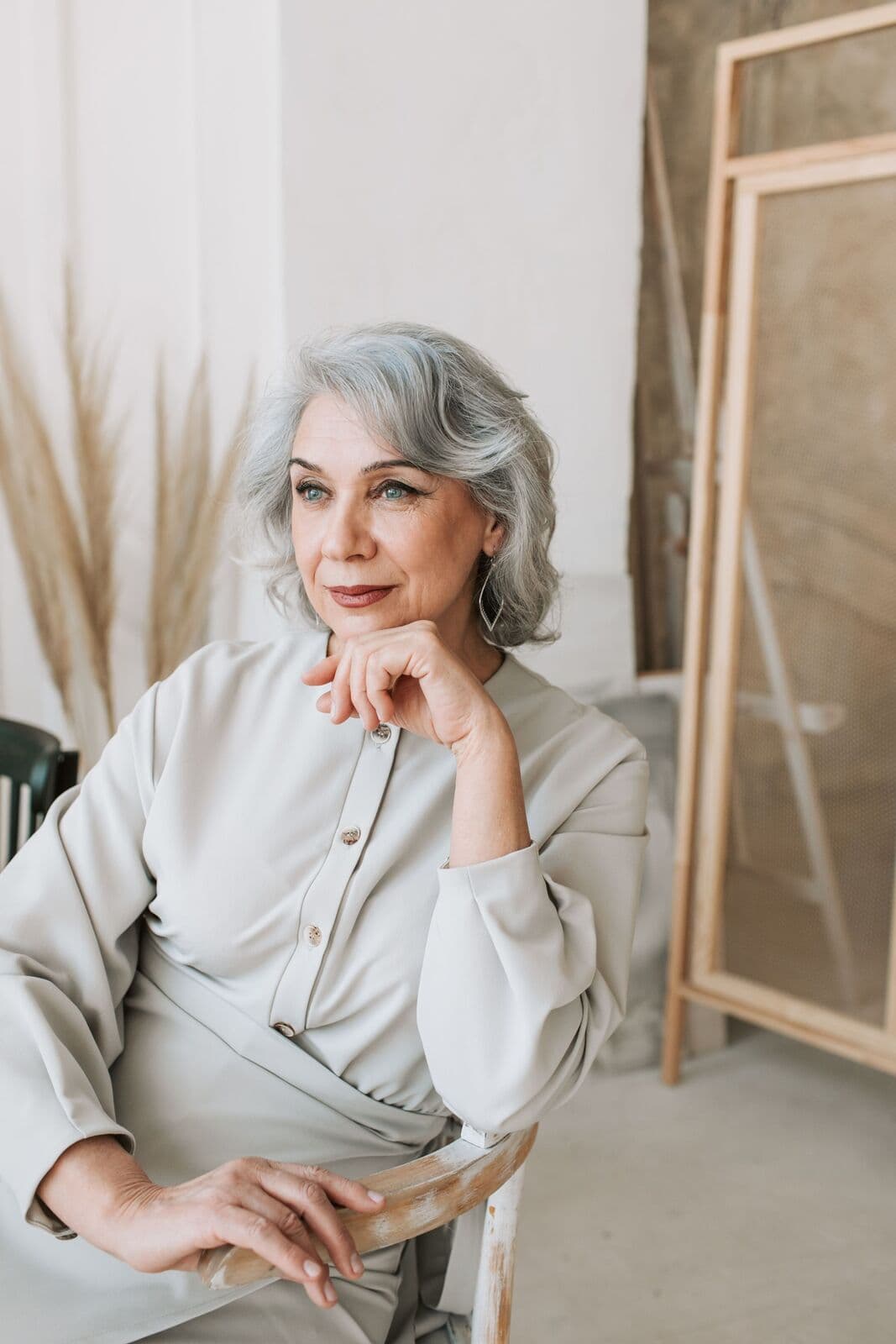 Woman in her sixties with silver hair seated in a pale dress