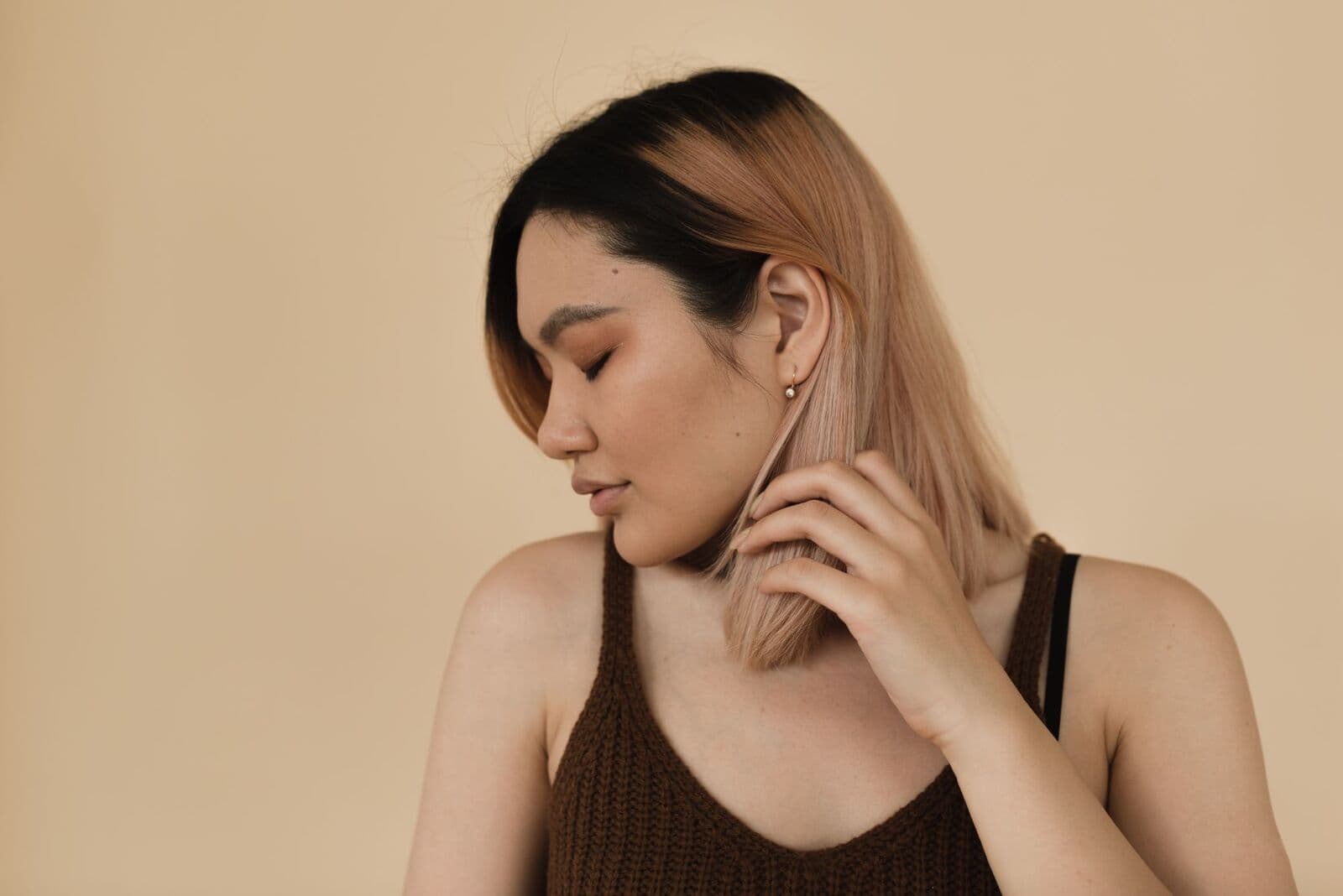 Woman with her eyes closed and a hand at her neck against a sand wall