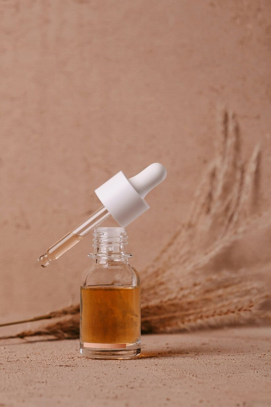 Clear dropper bottle of golden Face Oil against a clay wall
