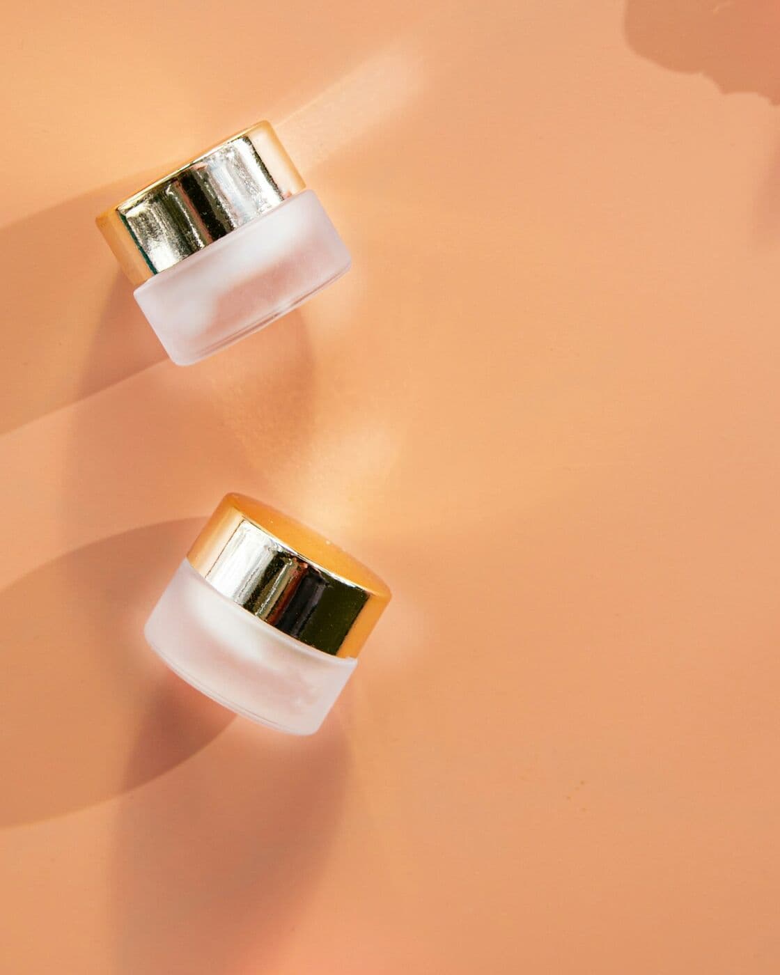 Two small frosted pots of Lip Balm SPF 15 on a peach surface