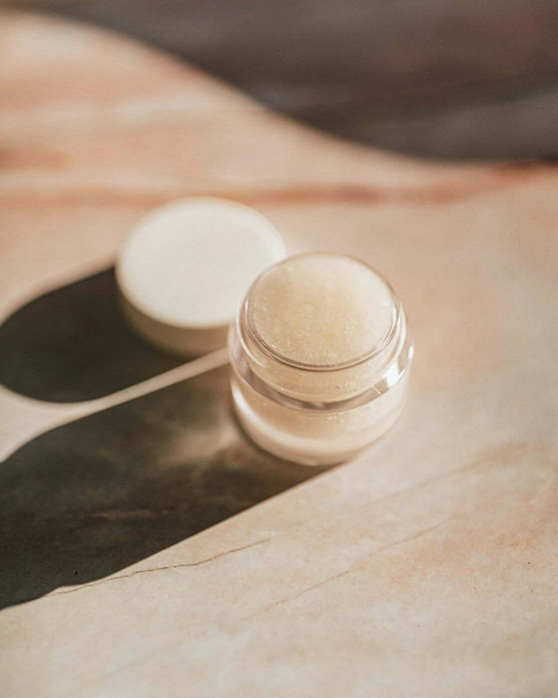 Small glass jar of Peptide Eye Cream open on a stone surface