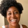 Woman with deep brown skin and a natural afro laughing in a white tank top