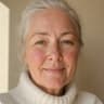 Woman in her sixties with silver hair pulled back and a flush on her cheeks, in a white turtleneck