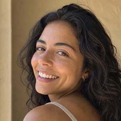 Young woman with long dark curls laughing over her shoulder in a beige tank top